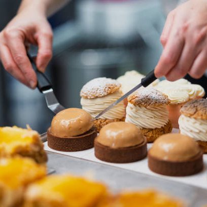 Close-up of a pastry chef's hands meticulously arranging delicious cream puffs and tarts on a tray, showcasing the artistry and precision of dessert making